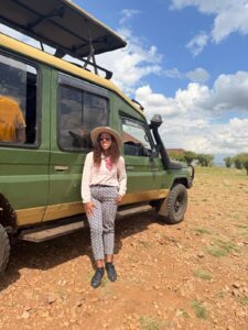 A woman stands in front of a safari bus in Africa. 